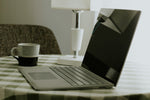 Laptop and coffee mug on a checkered tablecloth.