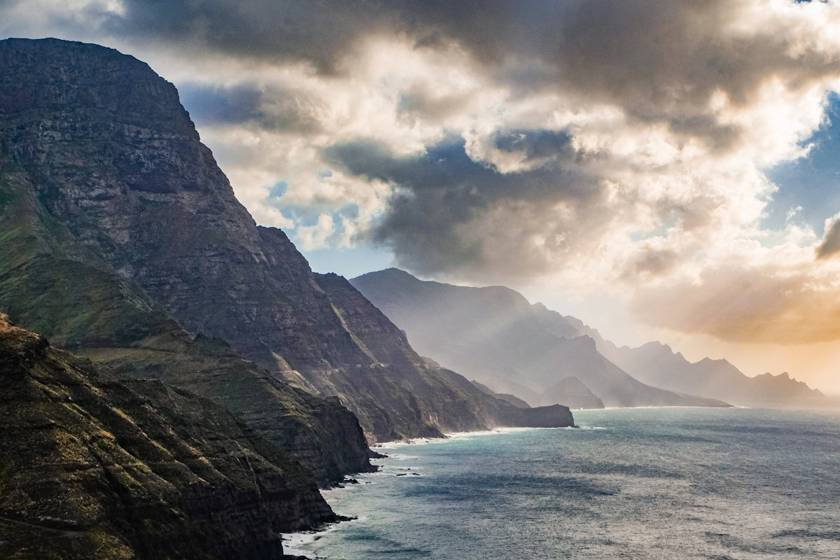 brown and green mountain beside body of water under cloudy sky during daytime