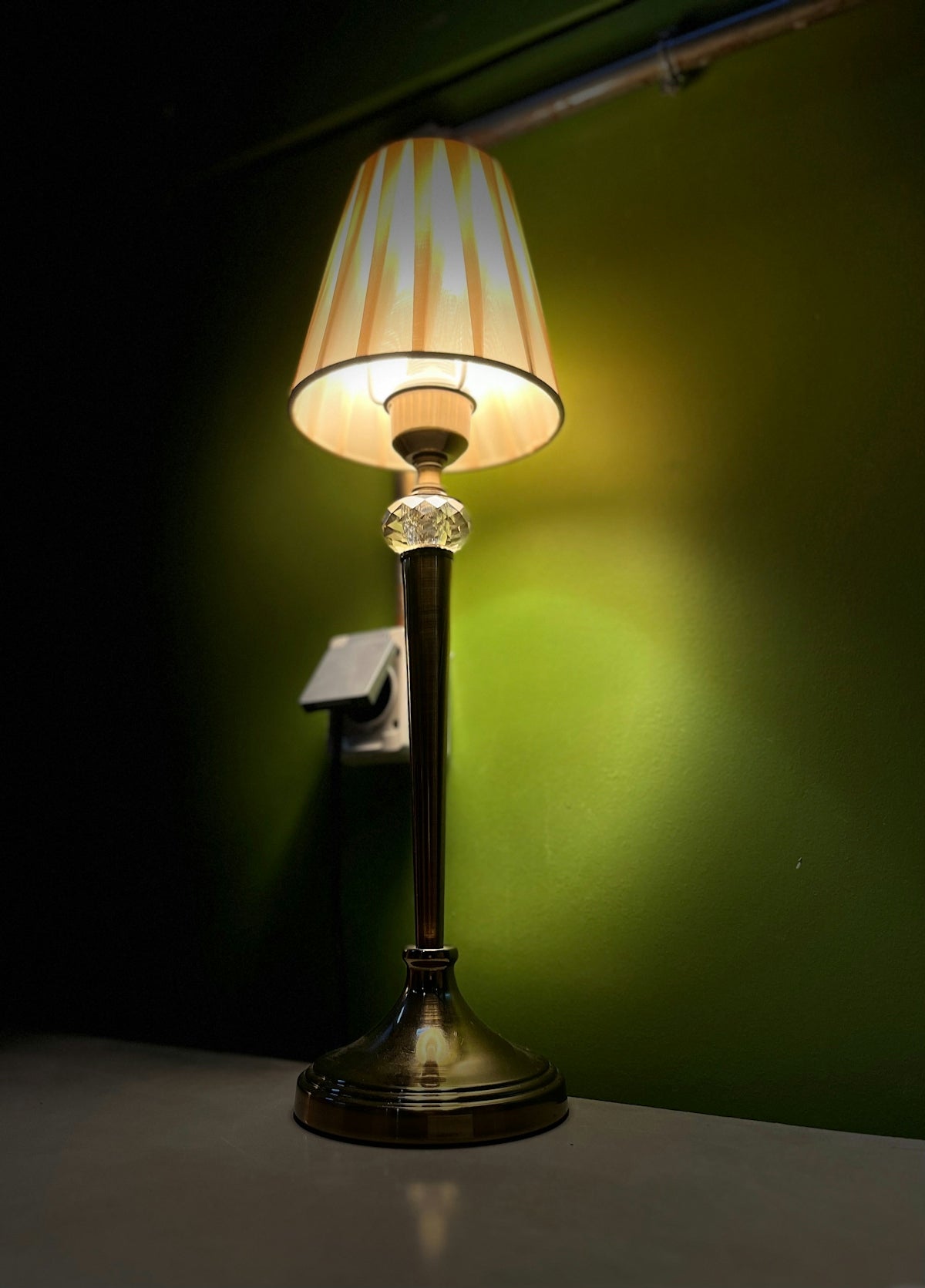 A lit lamp shines against a green wall.