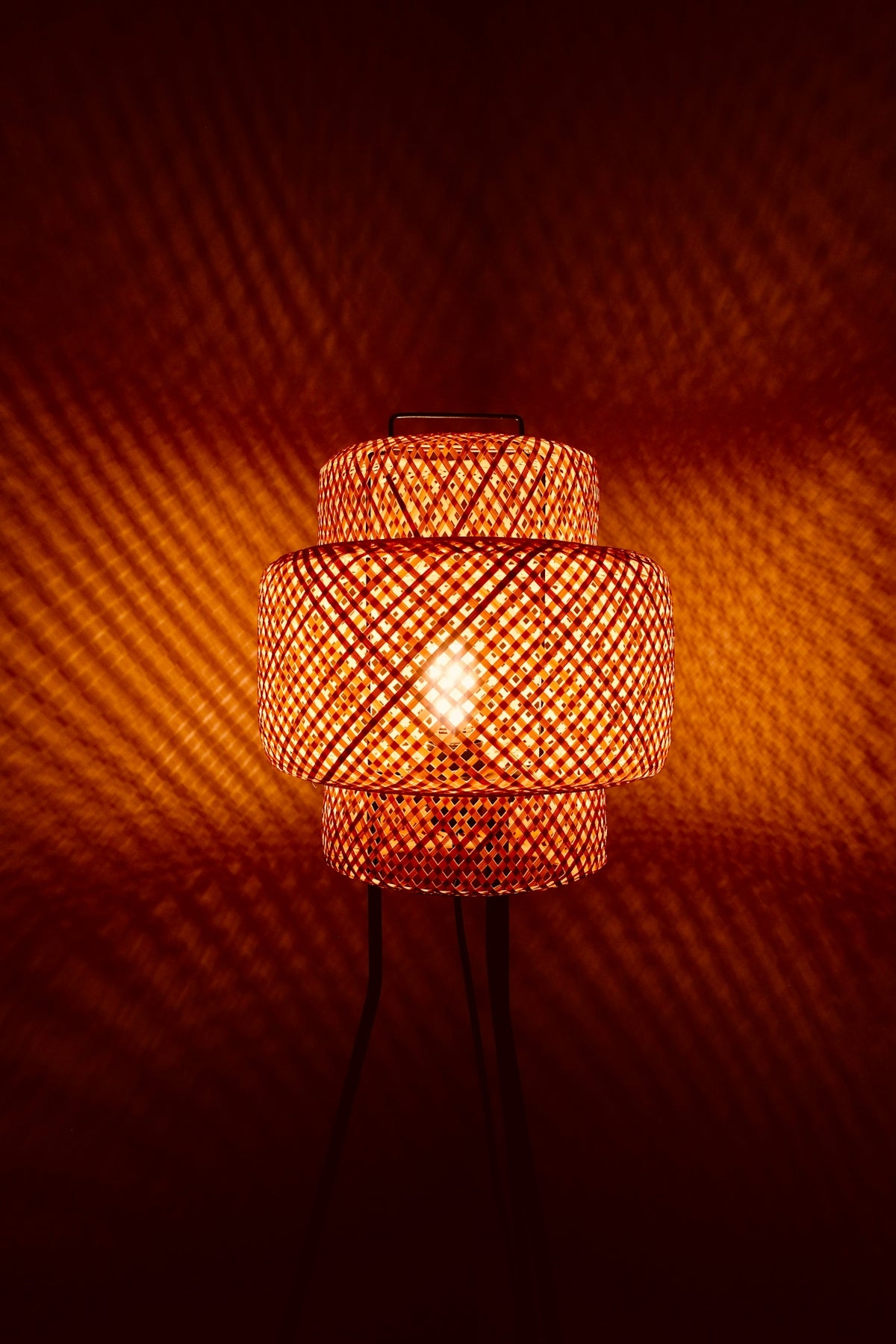 Woven bamboo lamp casting patterned light on wall
