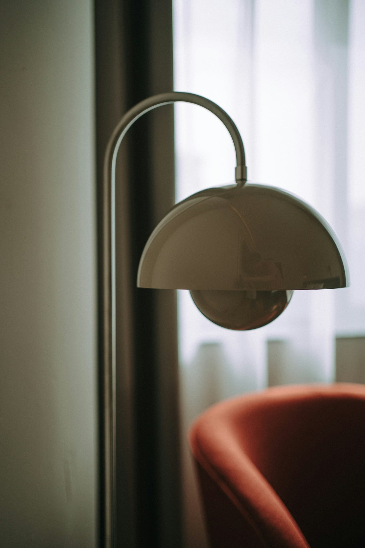 A modern floor lamp beside an orange armchair.