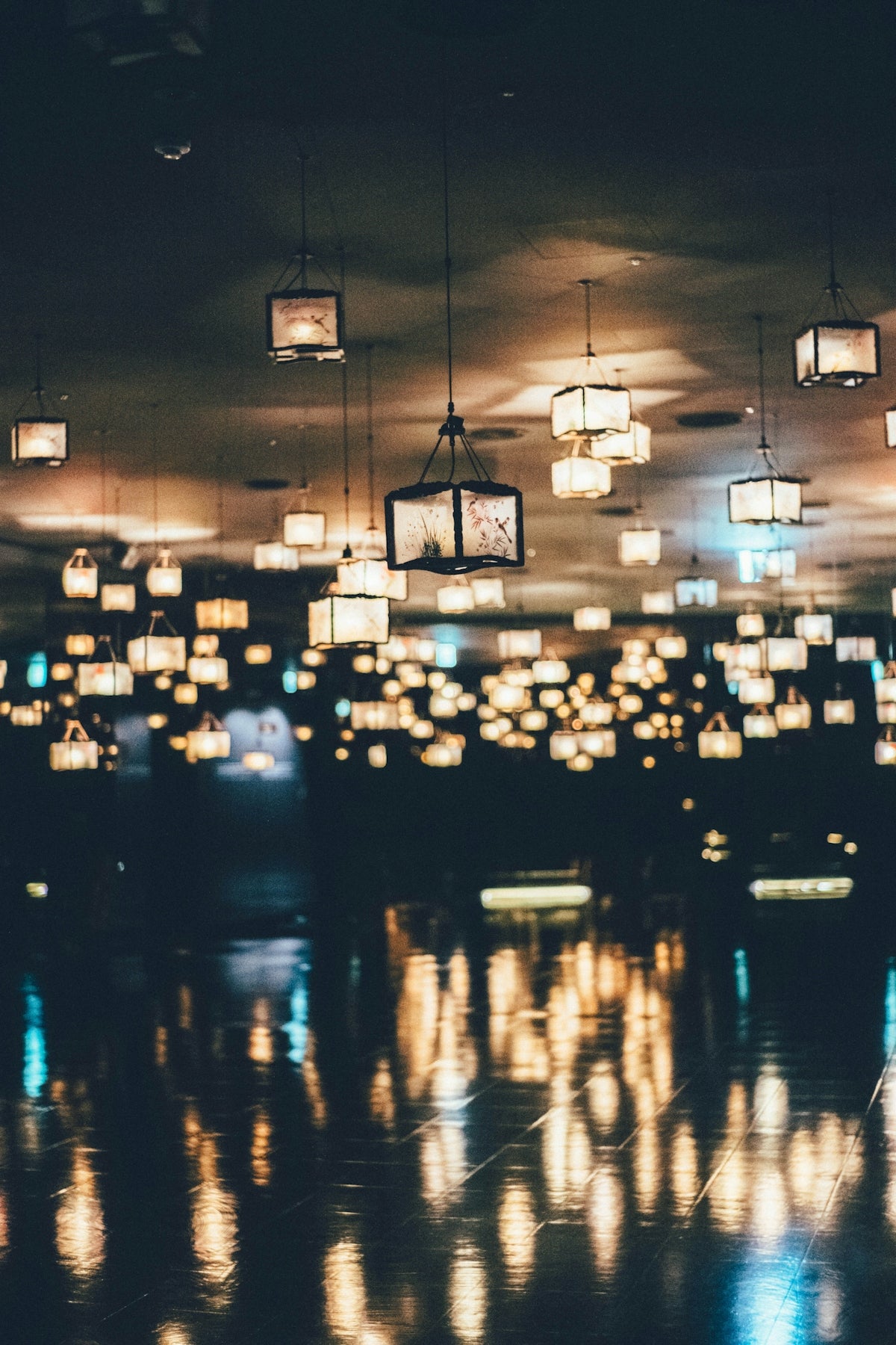 Many hanging lanterns illuminate a dark room with reflections.