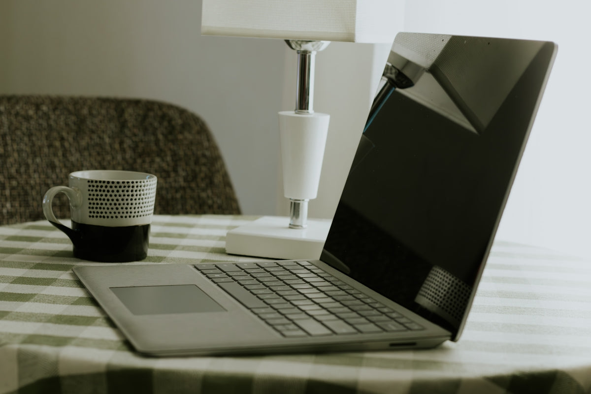 Laptop and coffee mug on a checkered tablecloth.