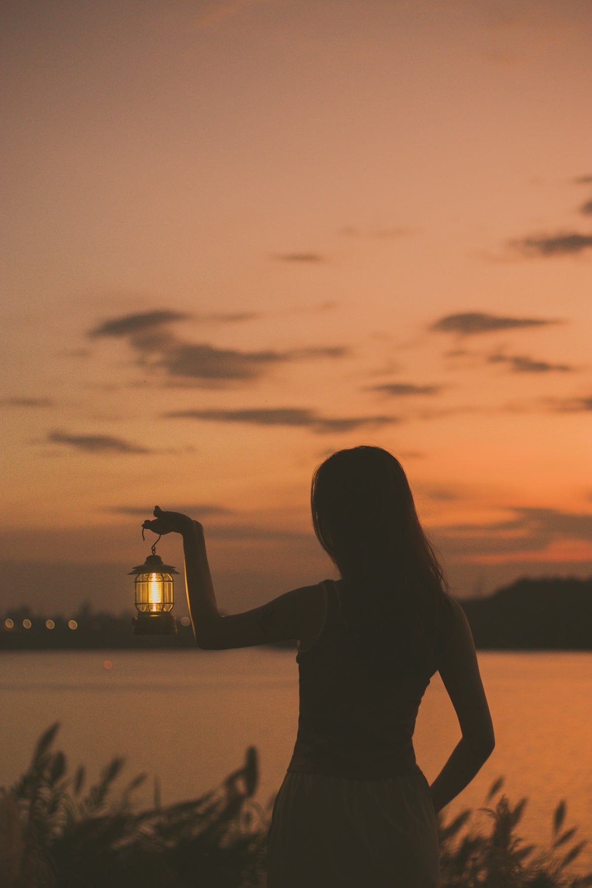 Silhouette of woman holding lantern at sunset