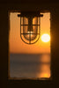 Industrial light fixture frames a sunset over the ocean