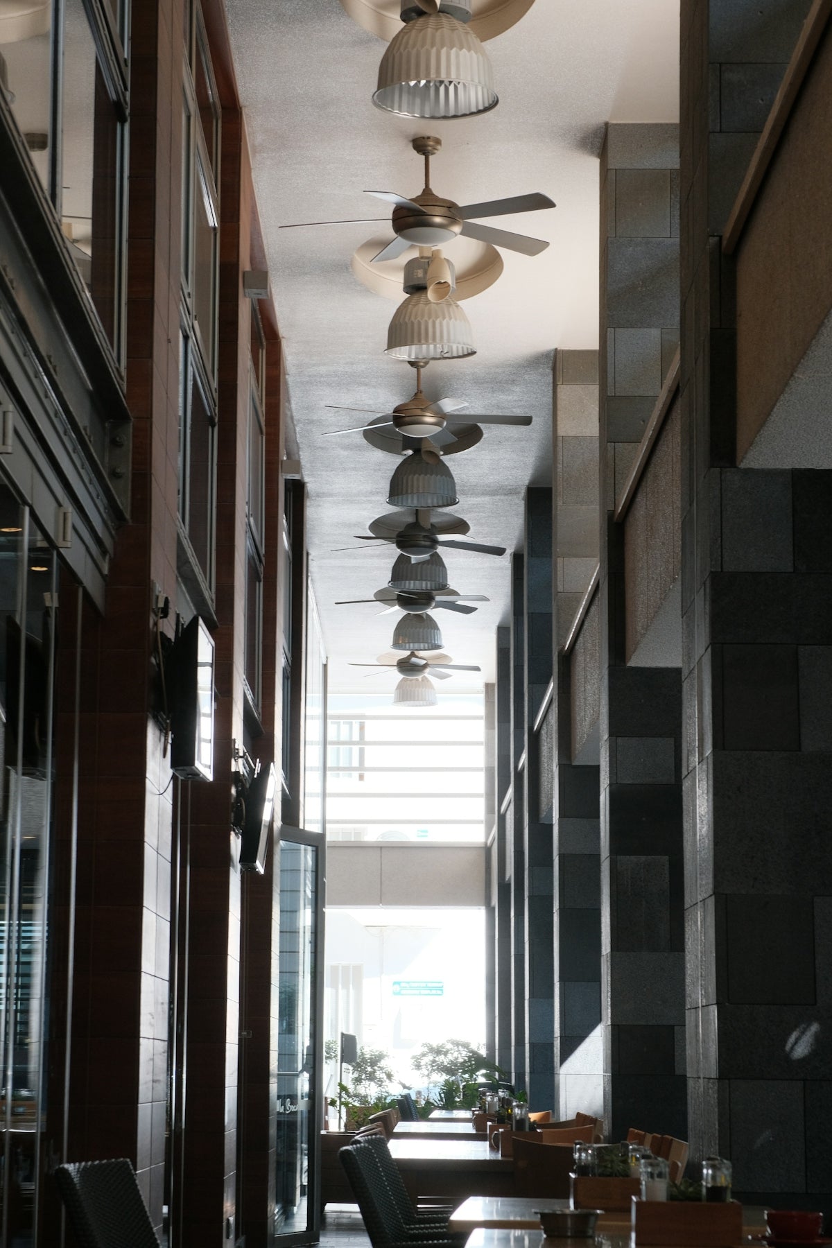 Ceiling fans line a modern hallway with tables below.