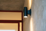 A modern black outdoor wall light illuminates concrete wall.