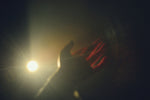 A hand reaching towards a bright light source.
