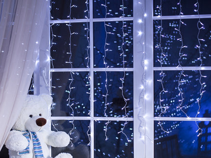 Cool white LED curtain lights draped over a window near a cute teddy bear for festive decor
