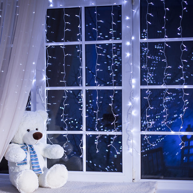 Cool white LED curtain lights draped over a window near a cute teddy bear for festive decor